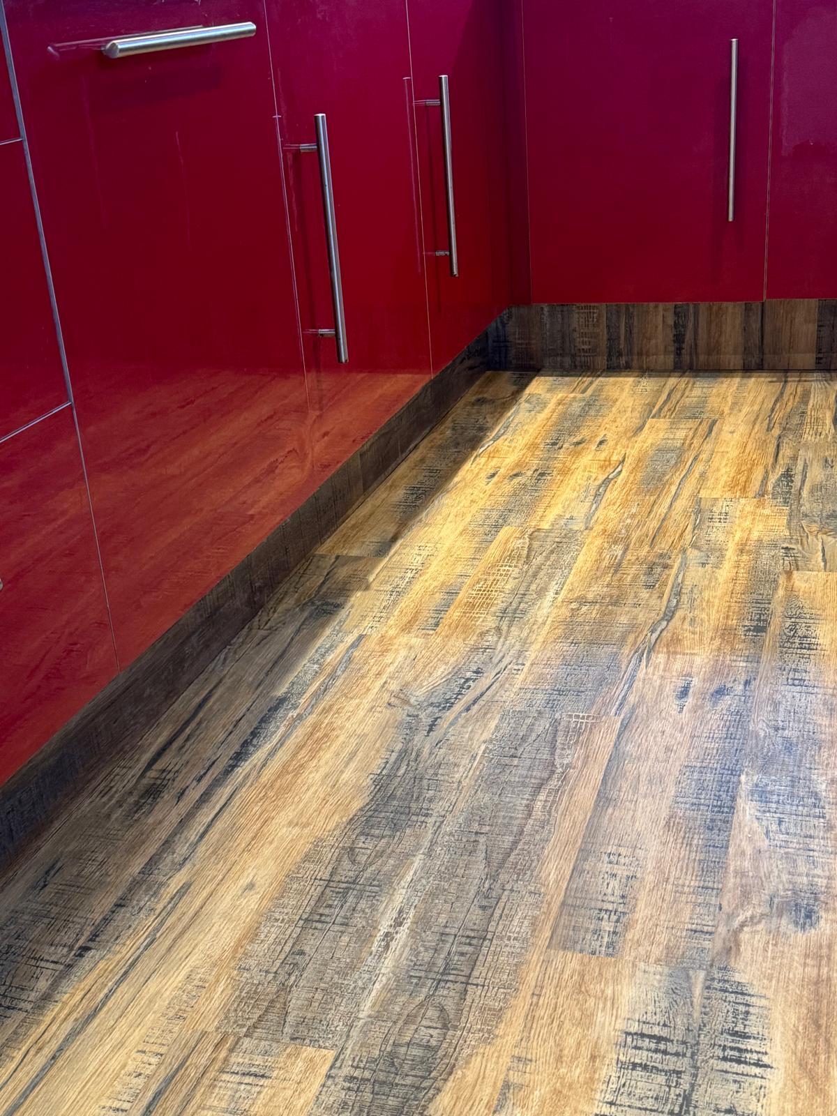 Rustic wood-effect flooring laid through a kitchen with high-gloss red units.